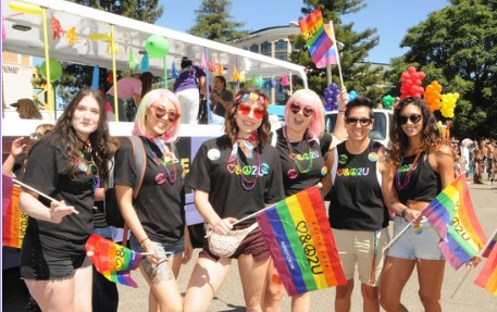 A crowd of people marching in a pride parade, holding signs and waving flags.